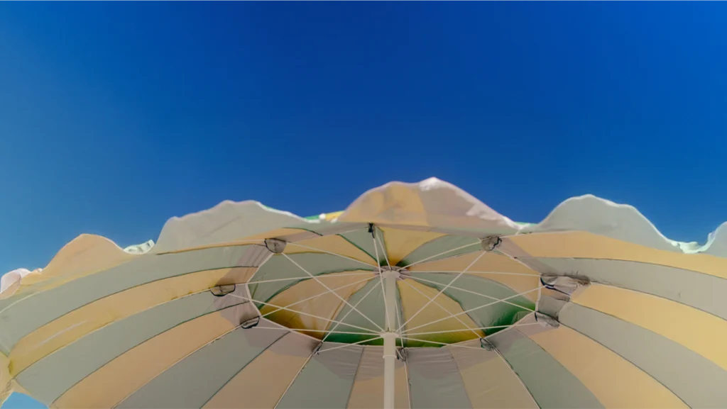 Yellow and light blue striped beach umbrella set against a clear blue sky.
