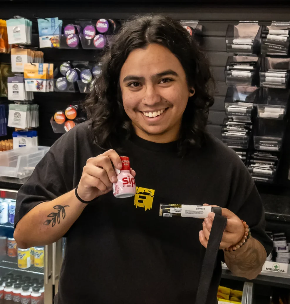 Story Cannabis budtender smiling and holding cannabis products while standing in front of the dispensary sales floor.