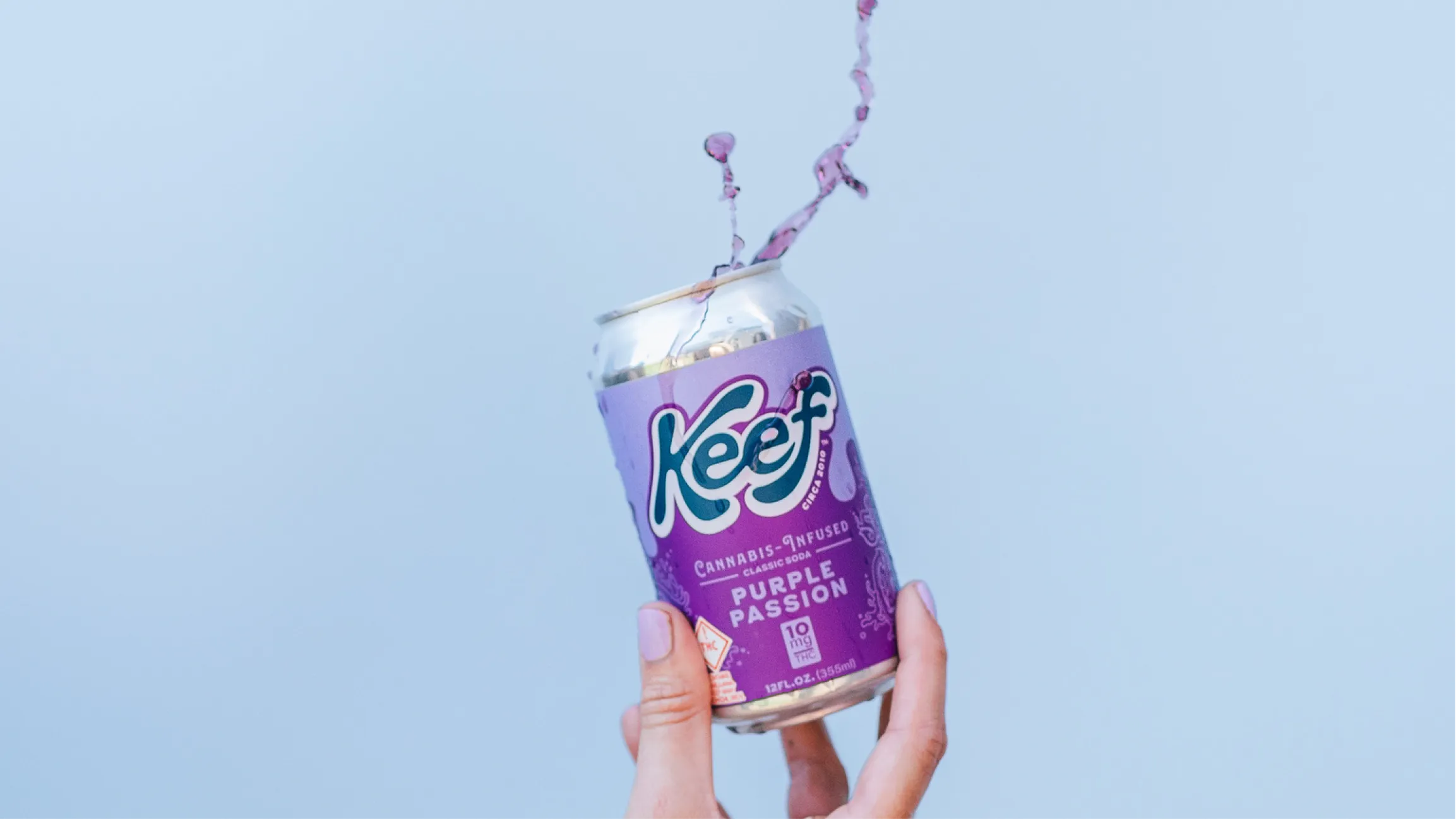 hand holding a keef cola purple passion drink with a splash